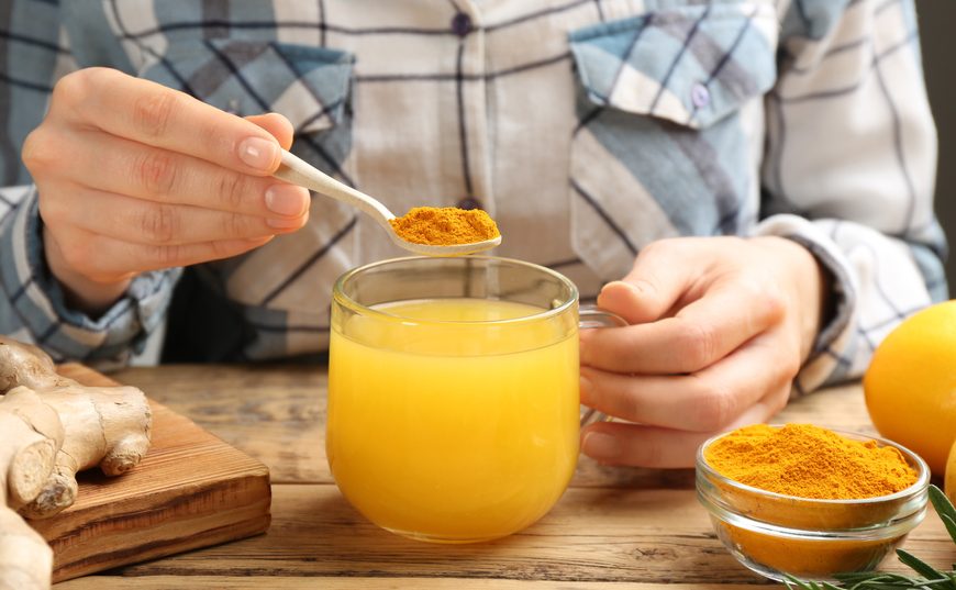 Woman,Adding,Turmeric,To,Immunity,Boosting,Drink,At,Wooden,Table