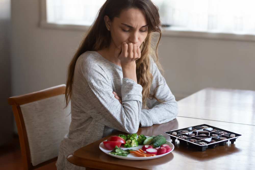 Unhappy,Young,Latin,Woman,Look,At,Chocolates,And,Vegetables,Face